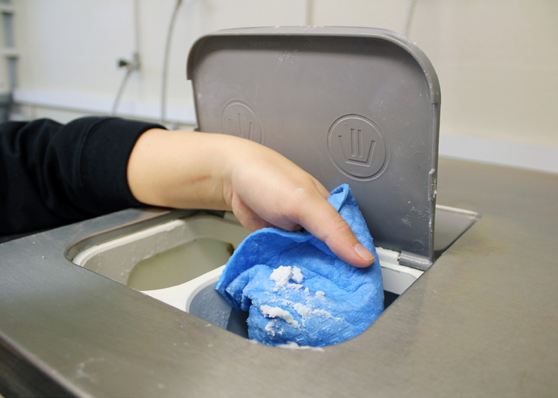Hand som håller i en disktrasa och torkar rent i tvättmedelsfacket på en tvättmaskin.