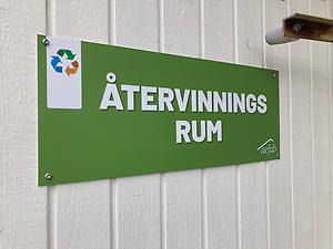 En grön skylt med texten "Återvinningsrum" sitter på en dörr.