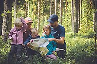 En familj är ute i skogen och läser tillsammans på en karta.